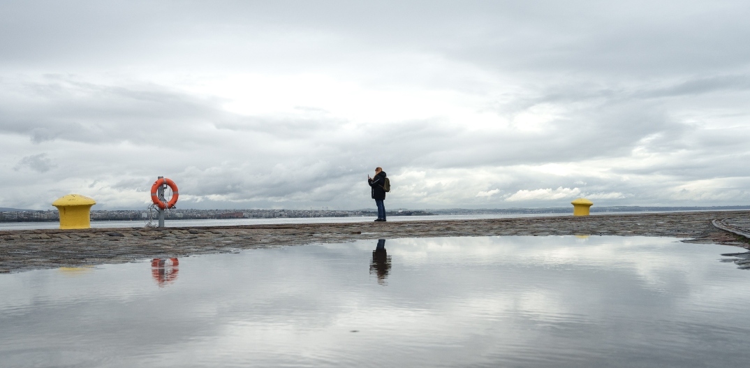 Γυναίκα στέκεται στην παραλία της Θεσσαλονίκης με συννεφιασμένο καιρό
