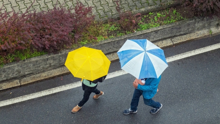 Δύο άνθρωποι περπατούν στον δρόμο κρατώντας ομπρέλα για τη βροχή