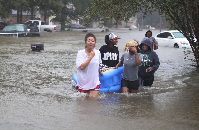 Άνθρωποι περπάτουν σε πλημμυρισμένο δρόμο αφού εγκατέλειψαν τα σπίτια τους