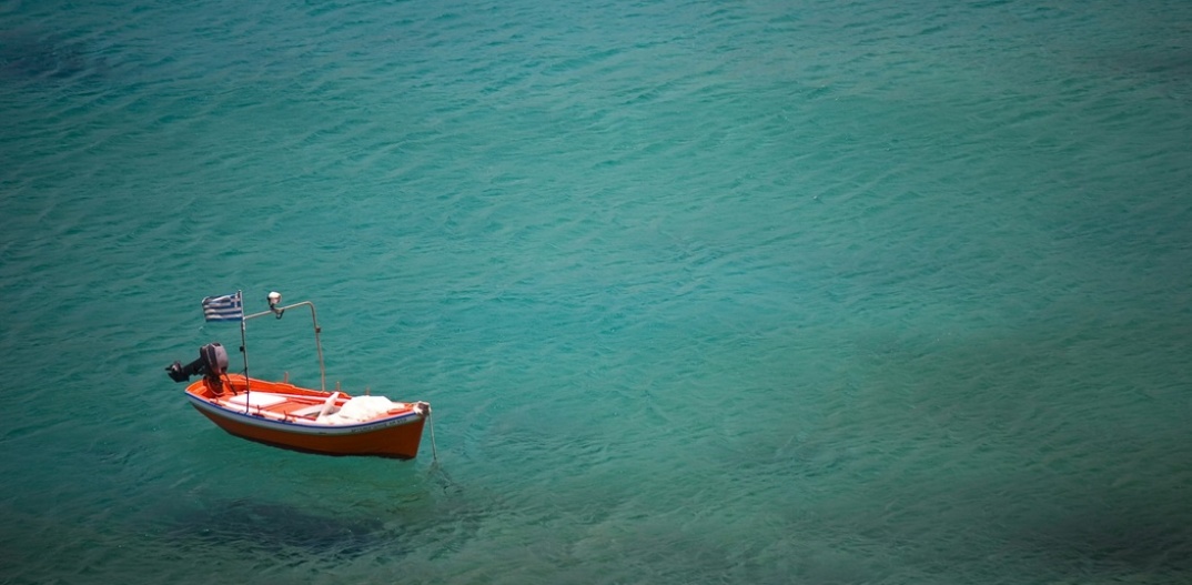 Παραλία και καΐκι αγκυροβολημένο που έχει στην πλώρη του την ελληνική σημαία
