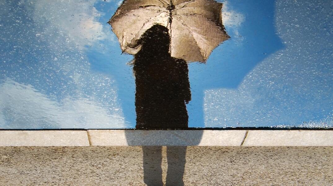 Άτομο με ομπρέλα  σε μία οθόνη με ψιχάλες και από πίσω ο ήλιος