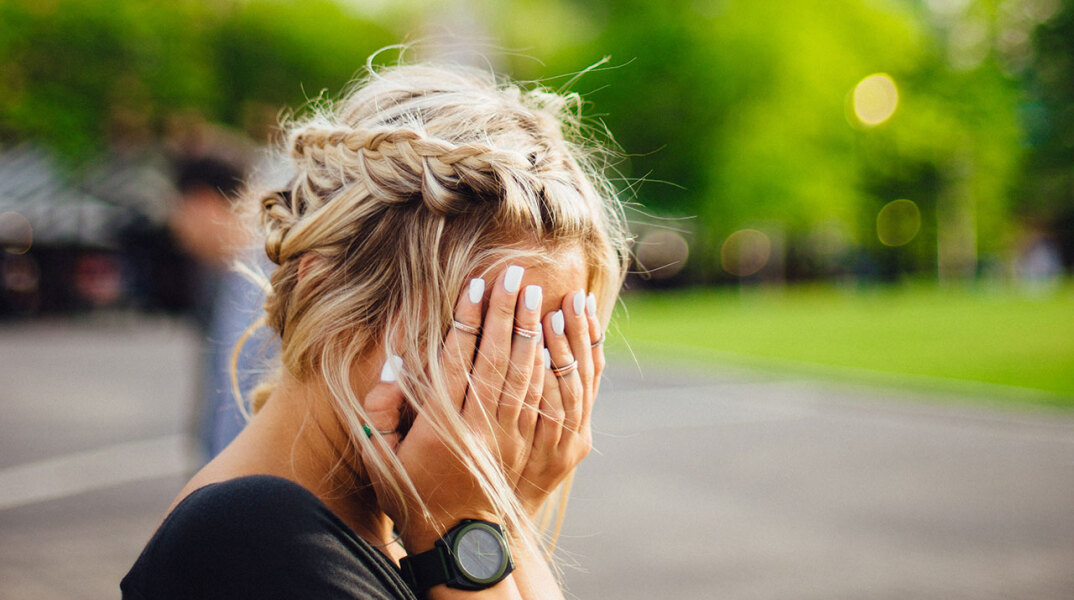 Κοπέλα κρύβει το πρόσωπό της με τα χέρια της