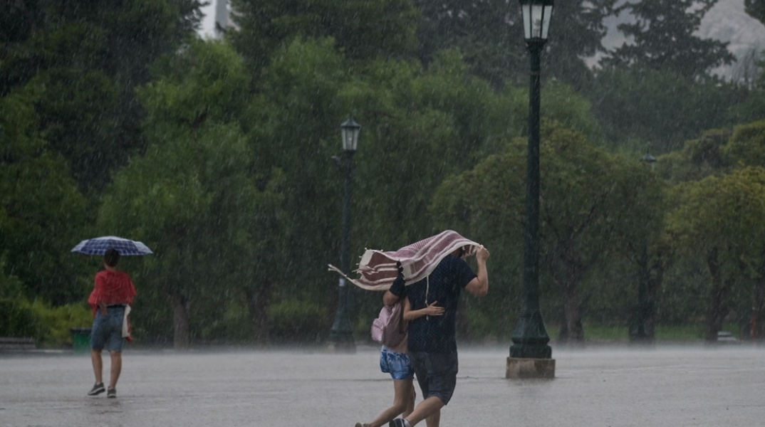 Καταιγίδα και ζευγάρι που περπατά αγκαλιασμένο προσπαθώντας να προφυλαχτεί