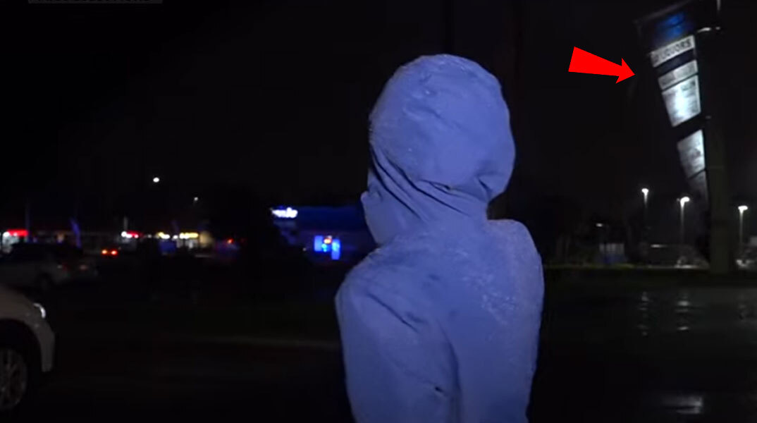 Η δημοσιογράφος στη Φλόριντα έχει γυρισμένη την πλάτη για να δει τον κυκλώνα Ίαν να ξηλώνει την πινακίδα στο εμπορικό κέντρο