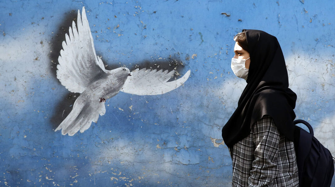 Γυναίκα με μαντίλα περνά μπροστά από mural στην Τεχεράνη