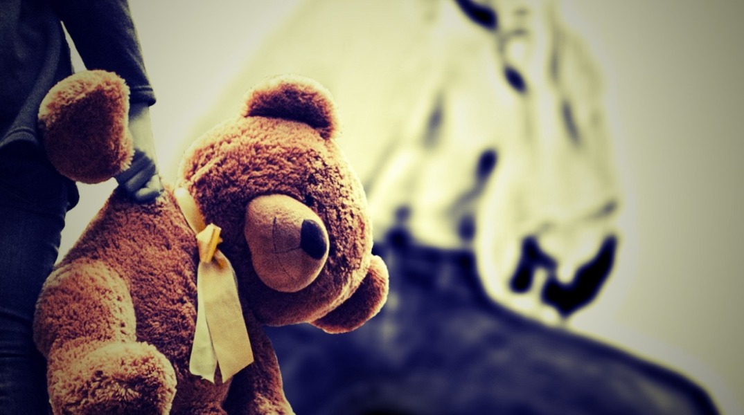 Παιδί με αρκουδάκι στα χέρια με φόντο σκιά που παραπέμπει σε κακοποίηση