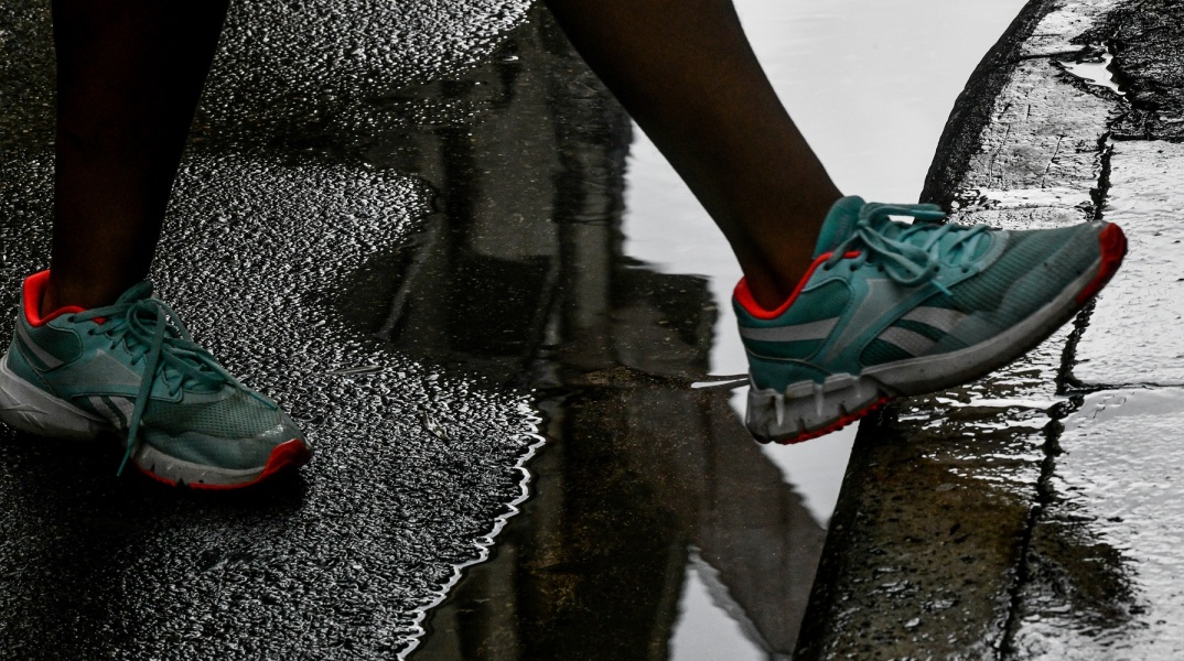 Πόδι με αθλητικό παπούτσι περνά πάω από λιμνάζοντα νερά σε δρόμο