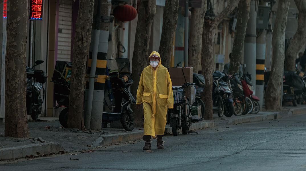 Κάτοικος στη Σανγκάη της Κίνας με αδιάβροχο και μάσκα για τον κορωνοϊό περπατά σε έρημο δρόμο της πόλης