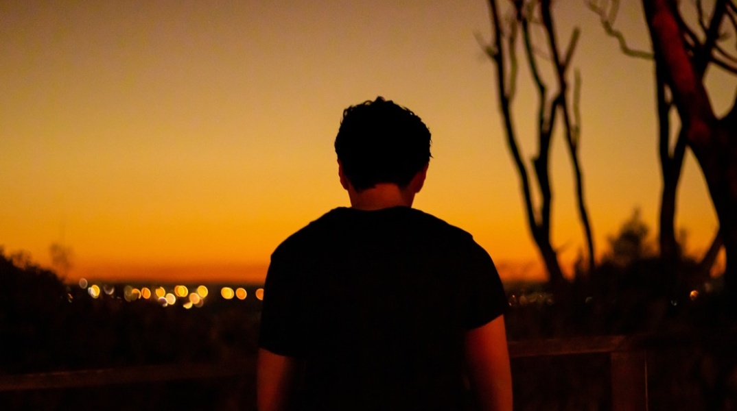 Νεαρό αγόρι με την πλάτη γυρισμένη στον φακό με το φως της δύσης του ήλιου