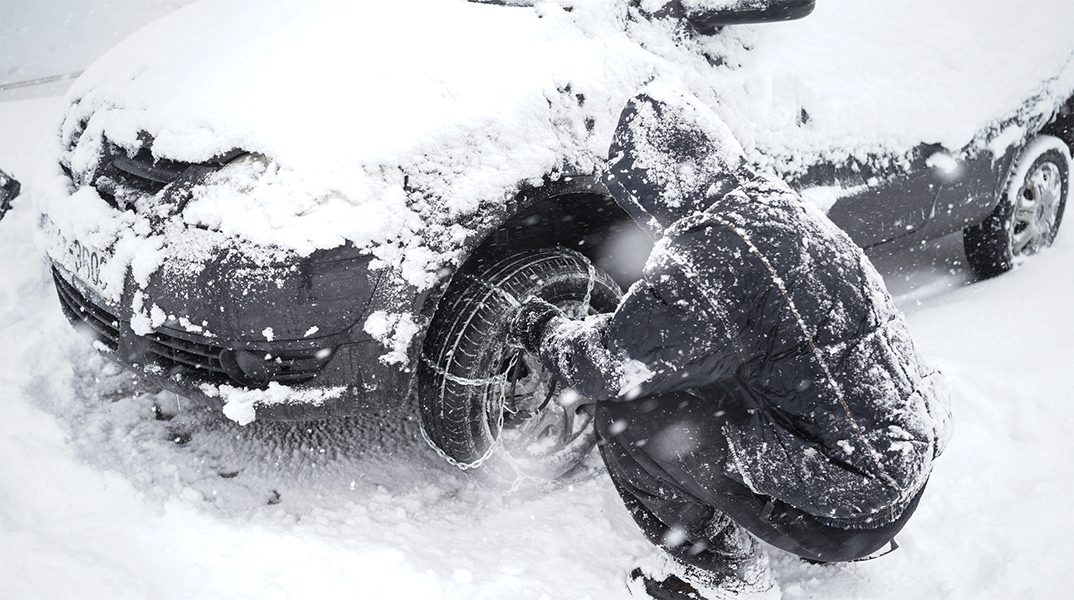 Άνδρας τοποθετεί αντιολισθητικές αλυσίδες στο όχημα του