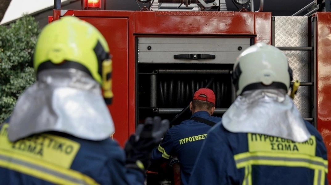 Πυροσβέστες φορούν τη στολή τους και στέκονται πίσω από όχημα, έτοιμοι να επιχειρήσουν για την κατάσβεση φωτιάς