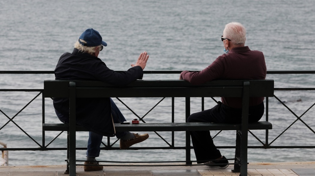 Συνταξιούχοι συνομιλούν ενώ κάθονται σε παγκάκι