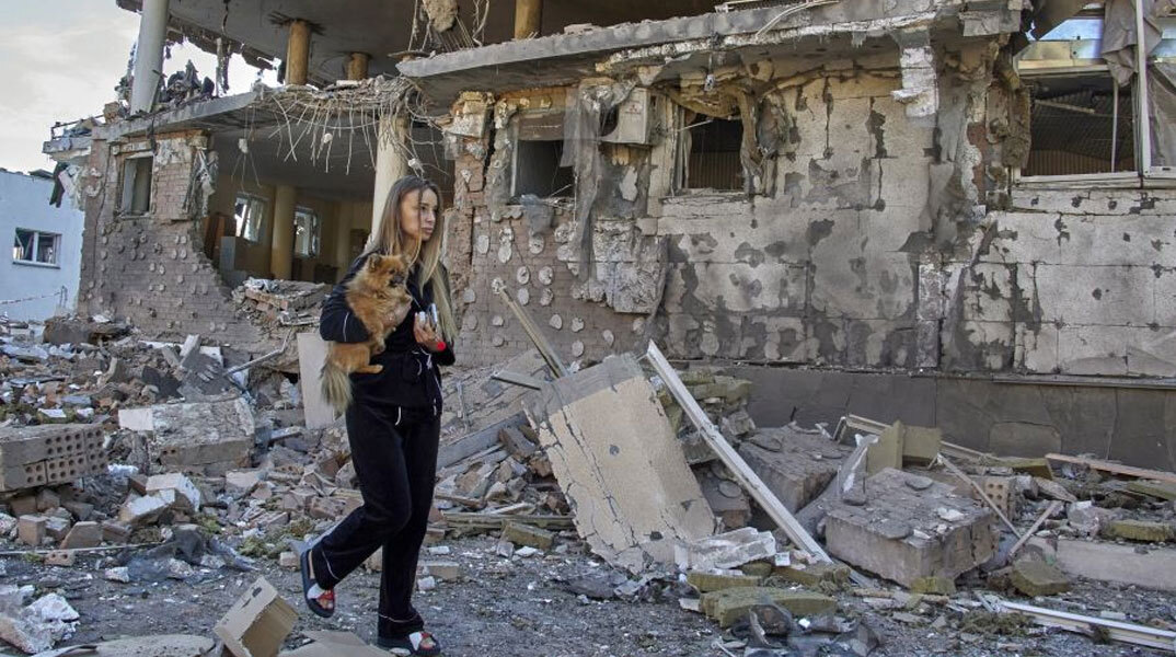 Νεαρή γυναίκα στο Χάρκοβο της Ανατολικής Ουκρανίας περνά μπροστά από βομβαρδισμένο κτίριο, κρατώντας στην αγκαλιά τη γάτα της