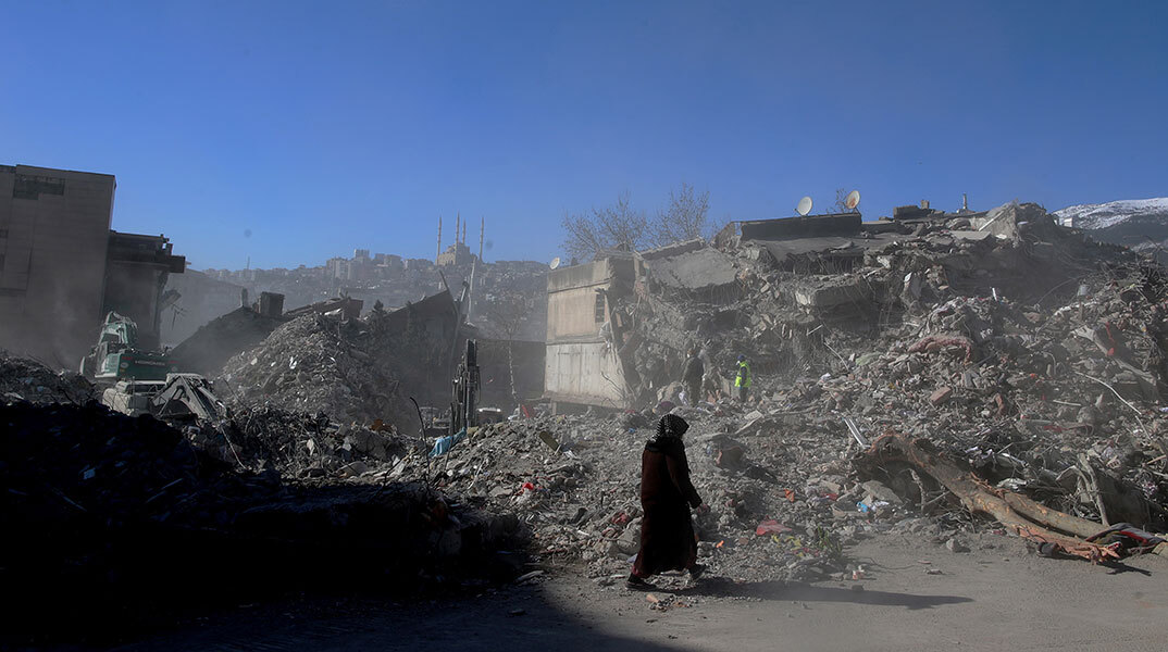 Γυναίκα ντυμένη στα μαύρα μπροστά από ισοπεδωμένα κτίρια στην πολη Καχραμανμαράς μετά τον σεισμό στην Τουρκία