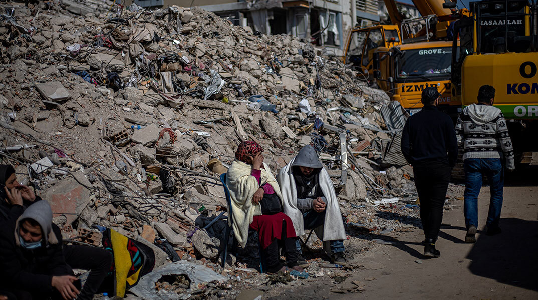Κάτοικοι στην πόλη Χατάι της Τουρκίας κάθονται δίπλα από έναν σωρό με ερείπια μετά τον σεισμό