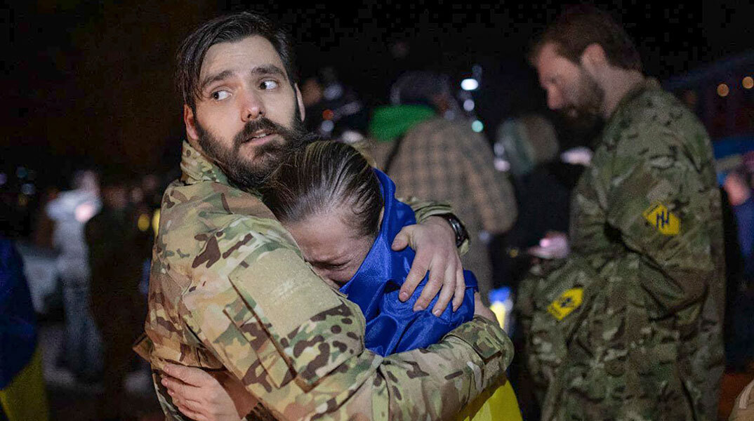Μητέρα με την ουκρανική σημαία στην πλάτη κλαίει στην αγκαλιά του γιου της, ο οποίος αφέθηκε ελεύθερος από τους Ρώσους στο πλαίσιο της ανταλλαγής αιχμαλώτων