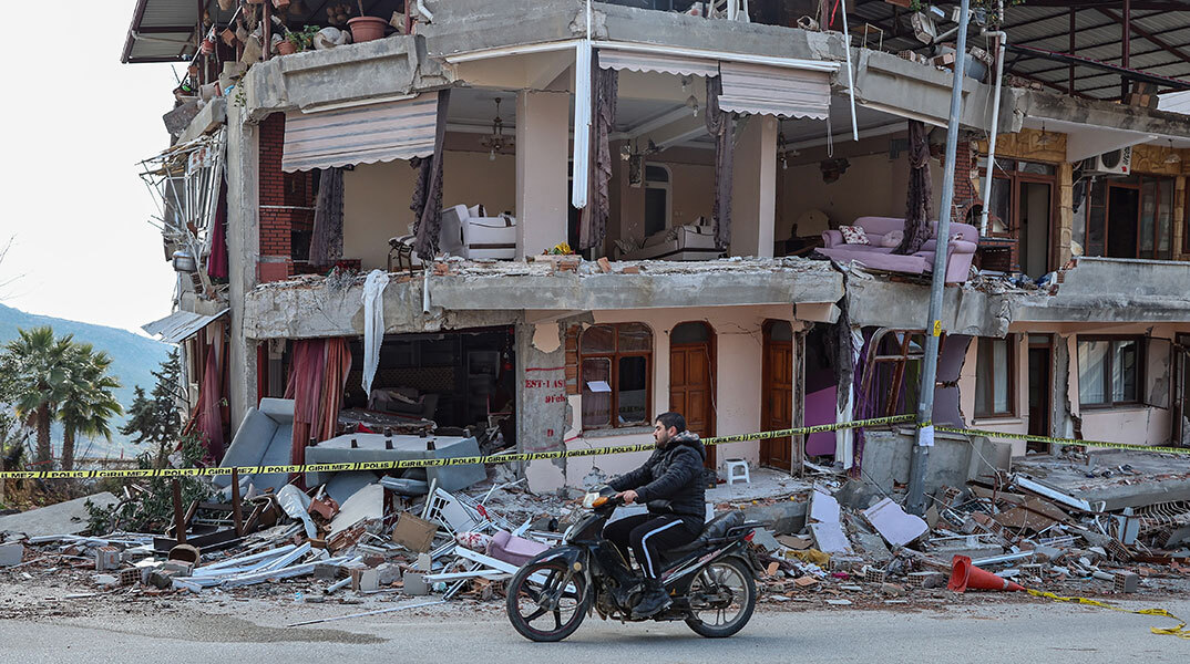 Νεαρός στην πόλη Χατάι περνά με το μηχανάκι μπροστά από κτίριο που έχει υποστεί ζημιές από τον σεισμό στην Τουρκία
