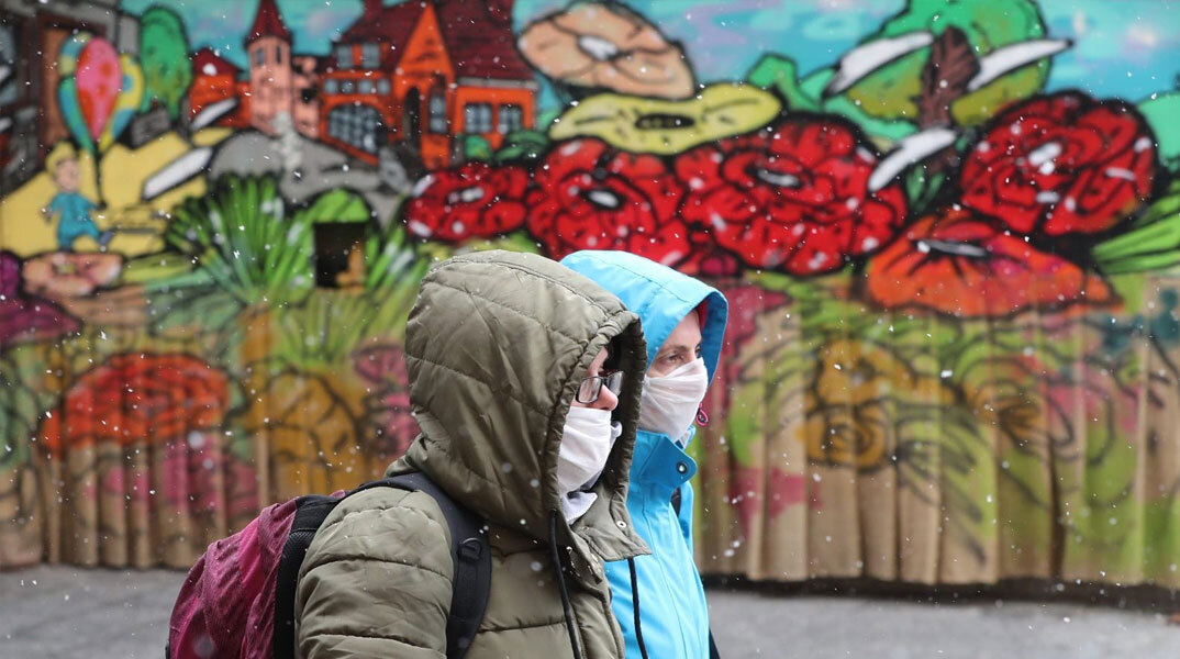 Άνθρωποι με μάσκα για τον κορωνοϊό μπροστά από mural για την πανδημία covid στο Σεράγεβο