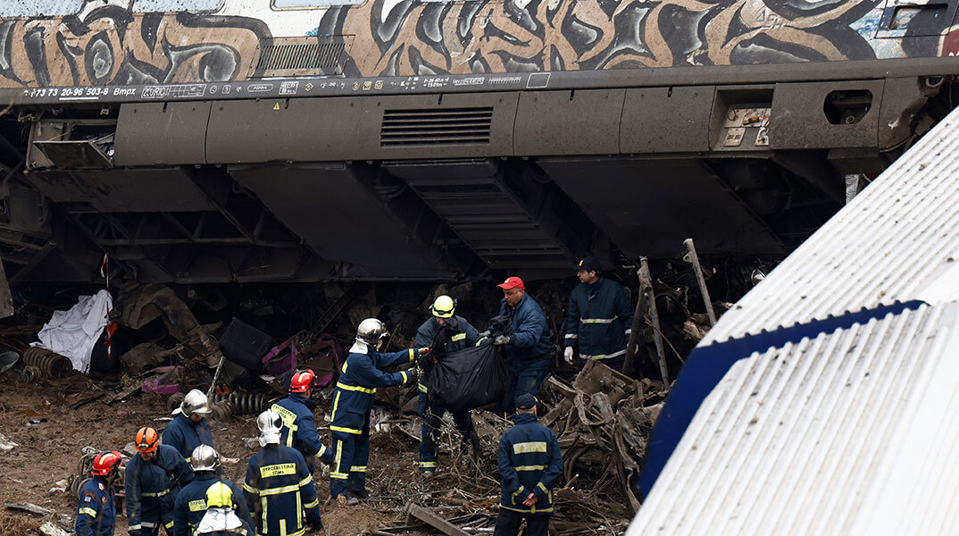 Πυροσβέστες απομακρύνουν τη σορό επιβάτη μετά τη σύγκρουση τρένων στα Τέμπη