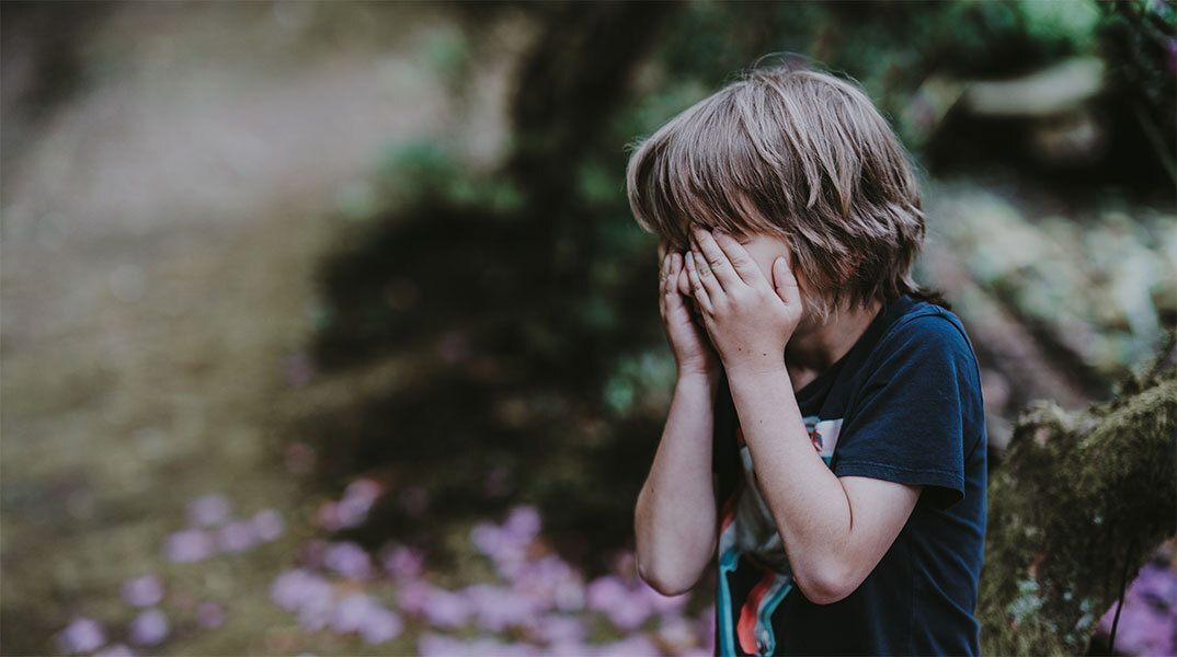 Ένα μικρό αγόρι κρύβει το πρόσωπό του με τα χέρια του