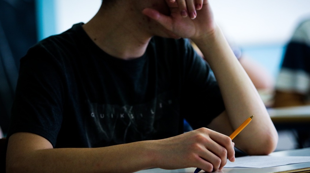 Μαθητής αναμένει στο θρανίο του για τα θέματα των εξετάσεων κρατώντας το στιλό στο χέρι