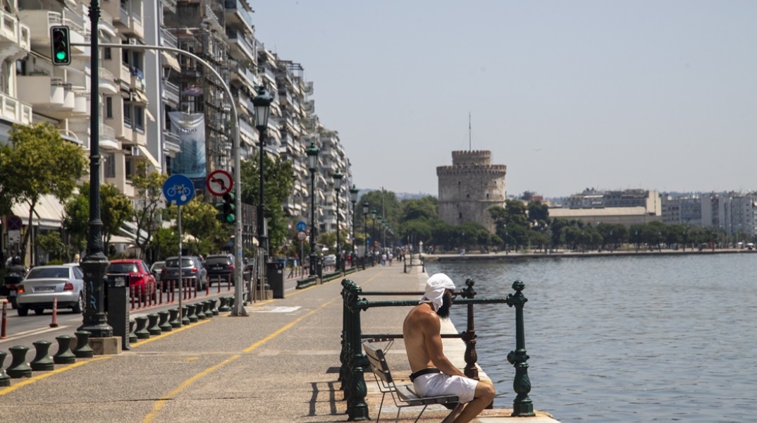 Πολίτης στη Θεσσαλονίκη καθισμένος σε παγκάκι εν μέσω καύσωνα φορά την μπλούζα του στο κεφάλι - Φόντο ο Λευκός Πύργος