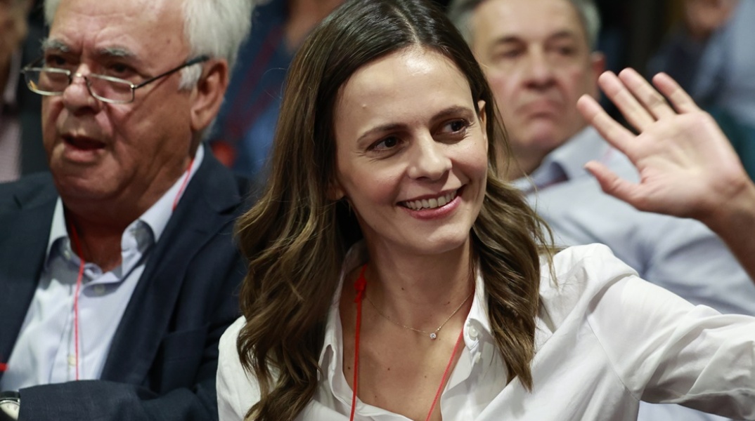 Η Έφη Αχτσιόγλου με σηκωμένο το χέρι χαιρετά και χαμογελά