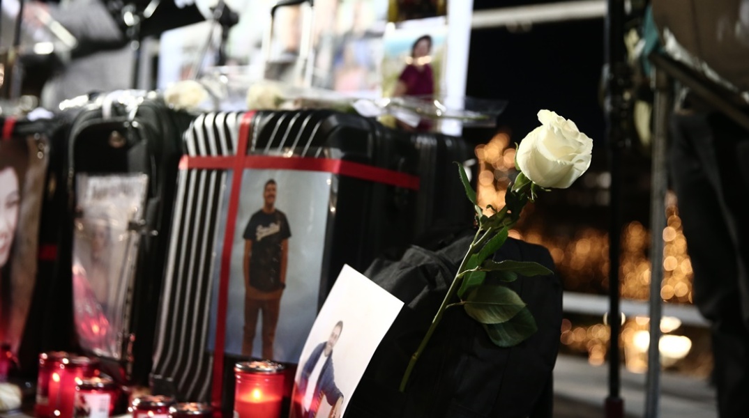 Κεριά, λευκά τριαντάφυλλα, λουλούδια και φωτογραφίες σε βαλίτσα στη μνήμη των θυμάτων της πολύνεκρης τραγωδίας στα Τέμπη
