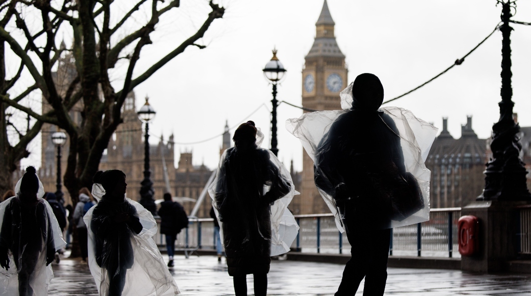 Κάτοικοι του Λονδίνου με αδιάβροχα μπροστά από το Παλάτι του Ουεστμίνστερ