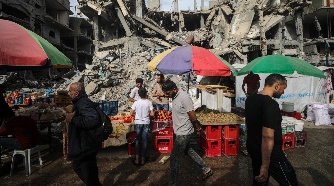 Διάφοροι Παλαιστίνιοι περνούν μπροστά από πάγκους με τρόφιμα που έχουν στηθεί δίπλα σε κατεστραμμένα κτίρια την τελευταία Παρασκευή του Ραμαζανιού κατά μήκος ενός δρόμου στον προσφυγικό καταυλισμό Al Nusairat, στη Λωρίδα της Γάζας