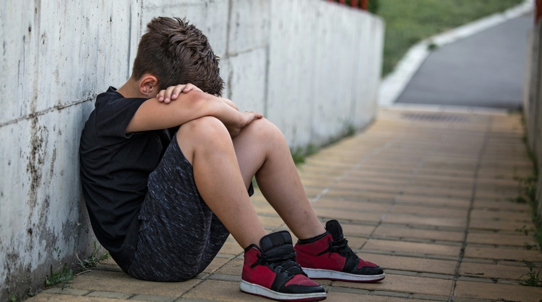 Νεαρό αγόρι κάθεται στο έδαφος σκυμμένο και κρύβει το πρόσωπό του