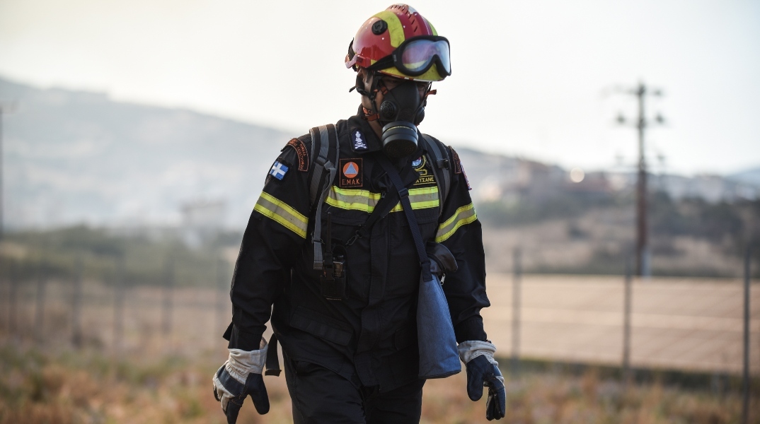 Πυροσβέστης με μπλε στολή, κράνος, μάσκα και γυαλιά προστασίας σε πυρκαγιά στην Λαμία