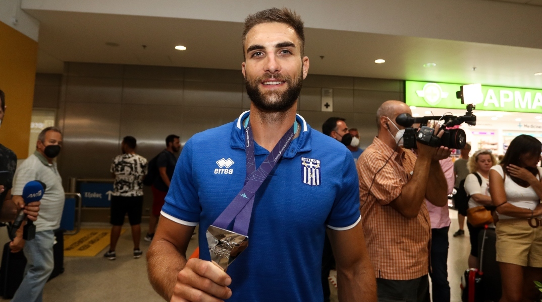 Ο Στέφανος Ντούσκος κρατώντας ένα μεταλλείο φορώντας μπλε αθλητική μπλούζα