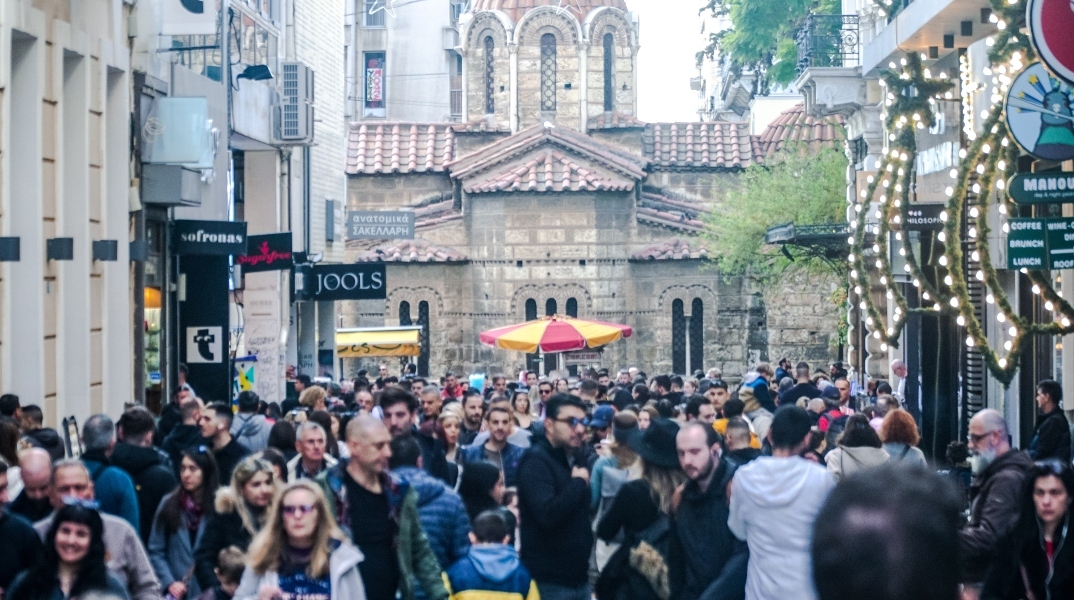 Πλήθος κόσμου περπατάει στην Ερμού μπροστά από μαγαζιά - Στο βάθος η εκκλησία Καπνικαρέα