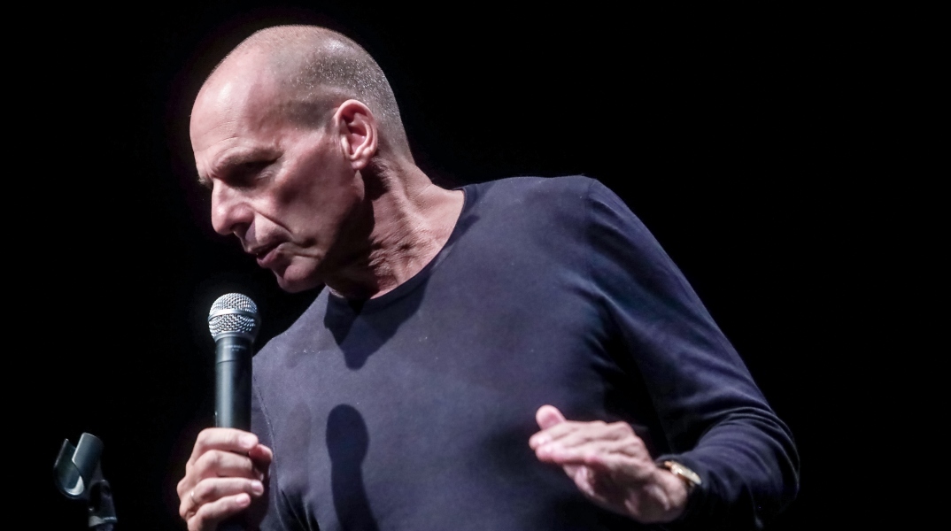 Ο Γιάννης Βαρουφάκης μιλάει όρθιος με μικρόφωνο