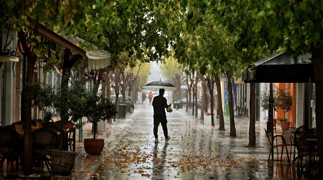 Άνδρας όρθιος με ομπρέλα στη μέση του δρόμου κατά την διάρκεια βροχής