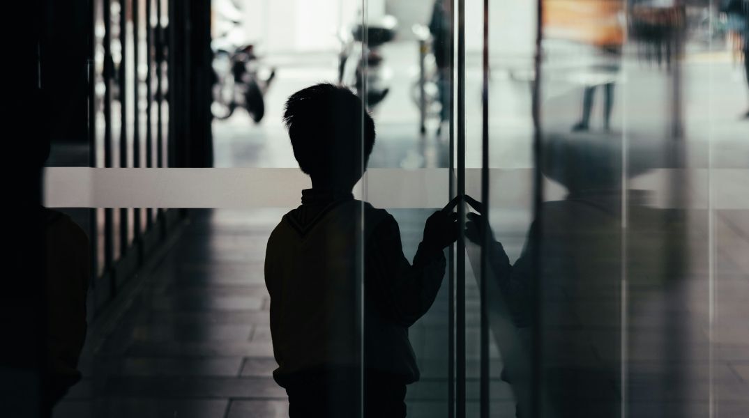 Σκιά ενός μικρού αγοριού που αγγίζει μια τζαμαρία έχοντας γυρισμένη την πλάτη στο φακό