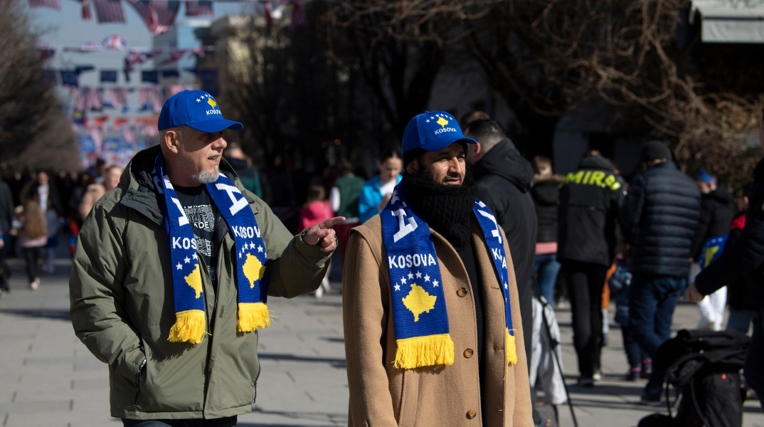 Δύο άντρες με κασκόλ και καπέλα που γράφουν Κόσοβο