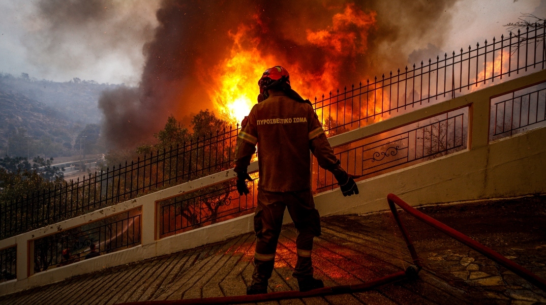 πυροσβέστης με καφέ στολή και μάσκα μπροστά από φωτιά
