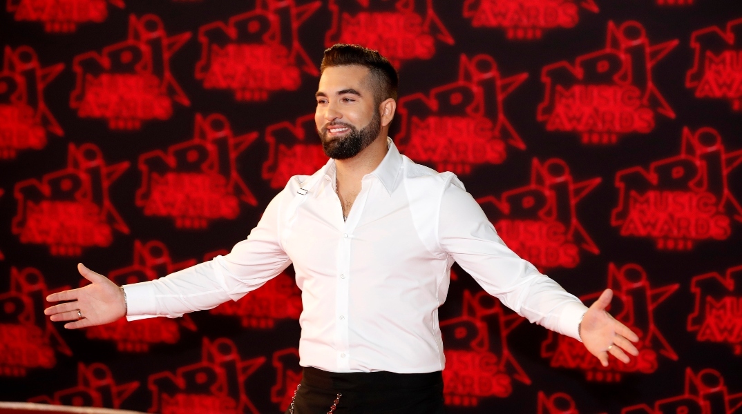 Ο Γάλλος τραγουδιστής Kendji Girac με ανοιχτά τα χέρια με άσπρο πουκάμισο και μαύρο παντελόνι