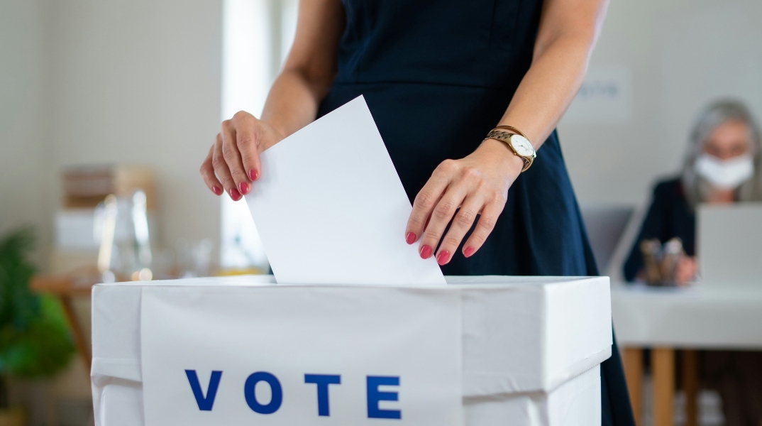 Γυναικεία χέρια ρίχνουν ψηφοδέλτιο σε κάλπη που γράφει vote