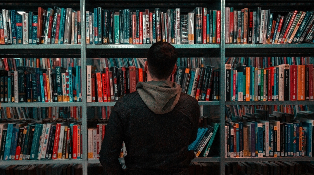 Άνδρας όρθιος μπροστά από βιβλιοθήκη γεμάτη βιβλία