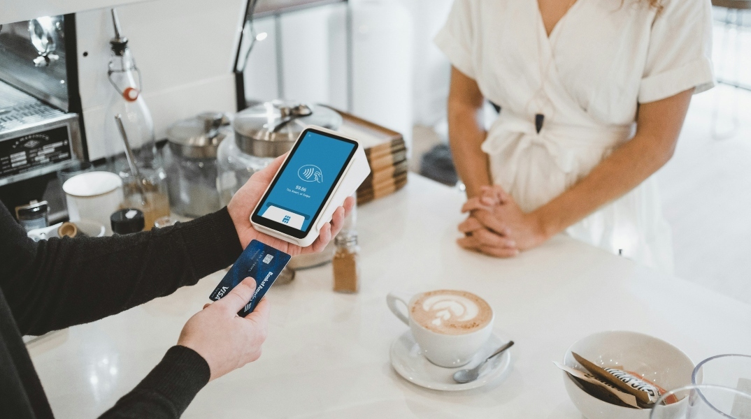 Δύο χέρια σκανάρουν κάρτα σε pos μπροστά από γυναίκα με άσπρο φόρεμα