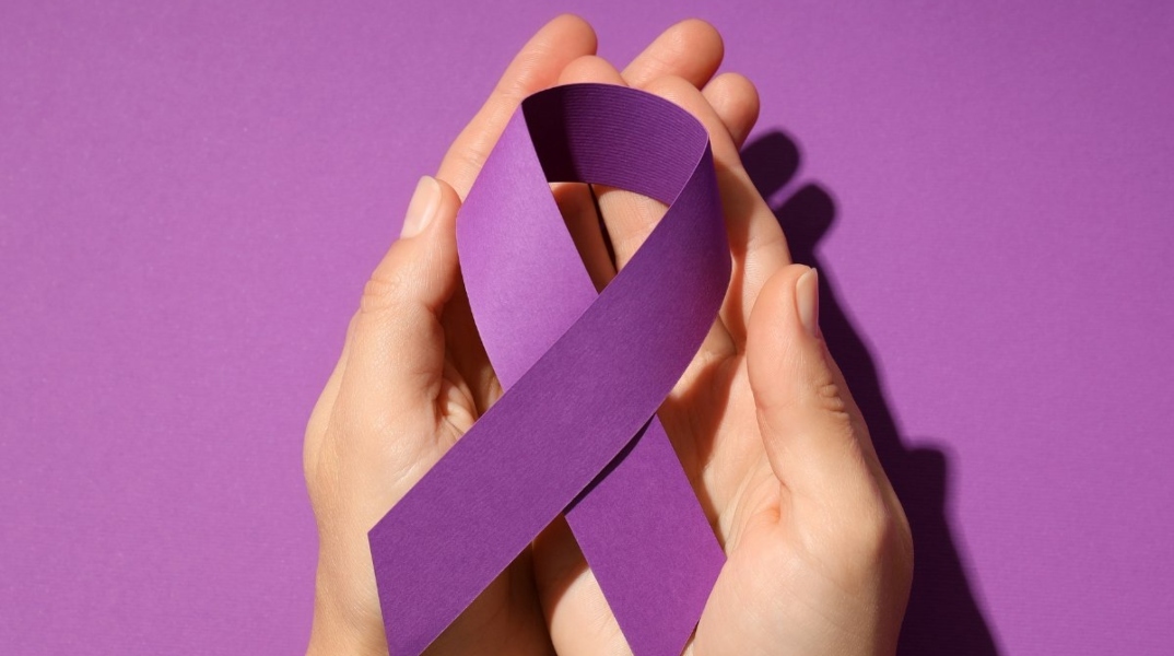 Δύο χέρια κρατάν μωβ κορδέλα