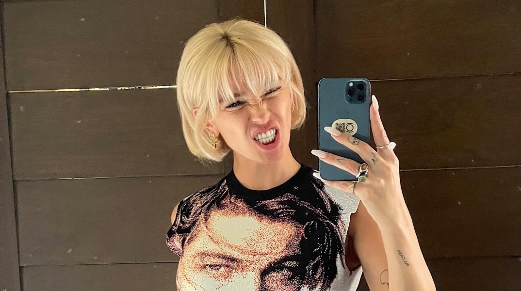 Ξανθιά γυναίκα κρατάει κινητό τηλέφωνο και χαμογελάει