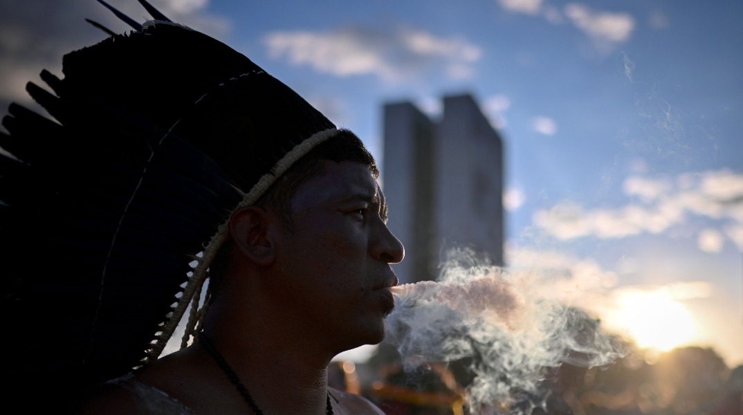 άνδρας με φτερά στο κεφάλι φυσάει καπνό - στο βάθος διπλή πολυκατοικία