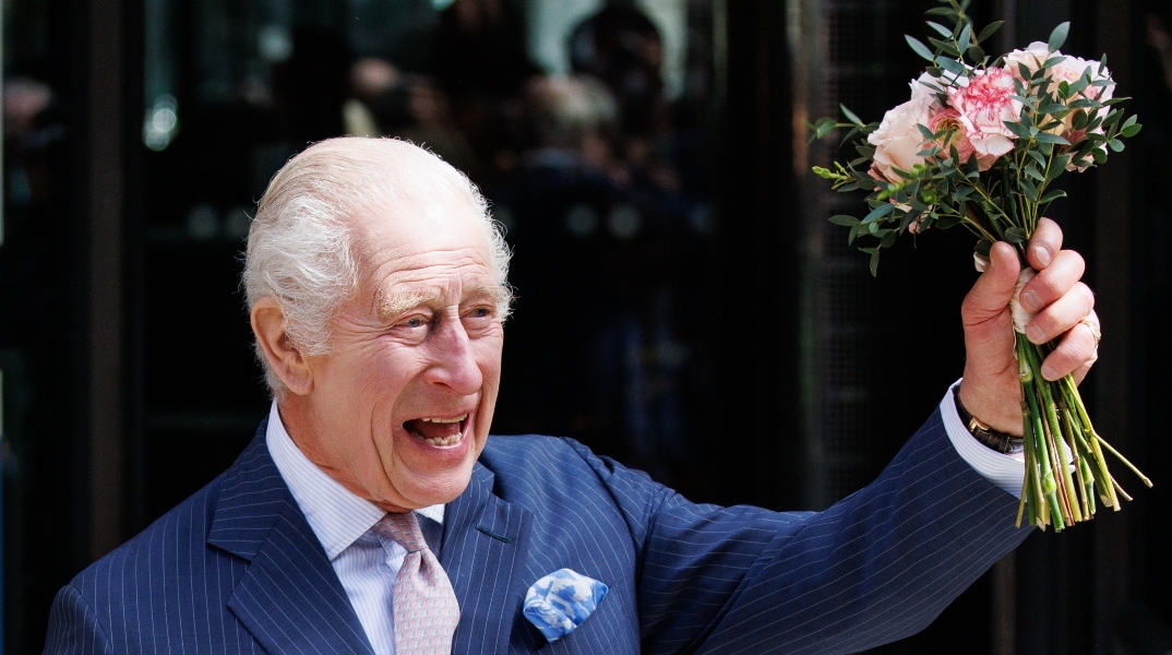 Άνδρας με ριγέ μπλε σακάκι χαμογελάει κρατώντας λουλούδια