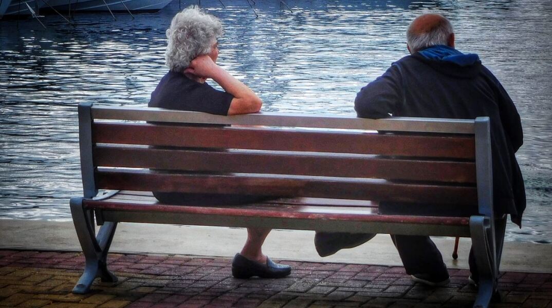 Συνταξιούχοι σε παγκάκι με φόντο τη θάλασσα