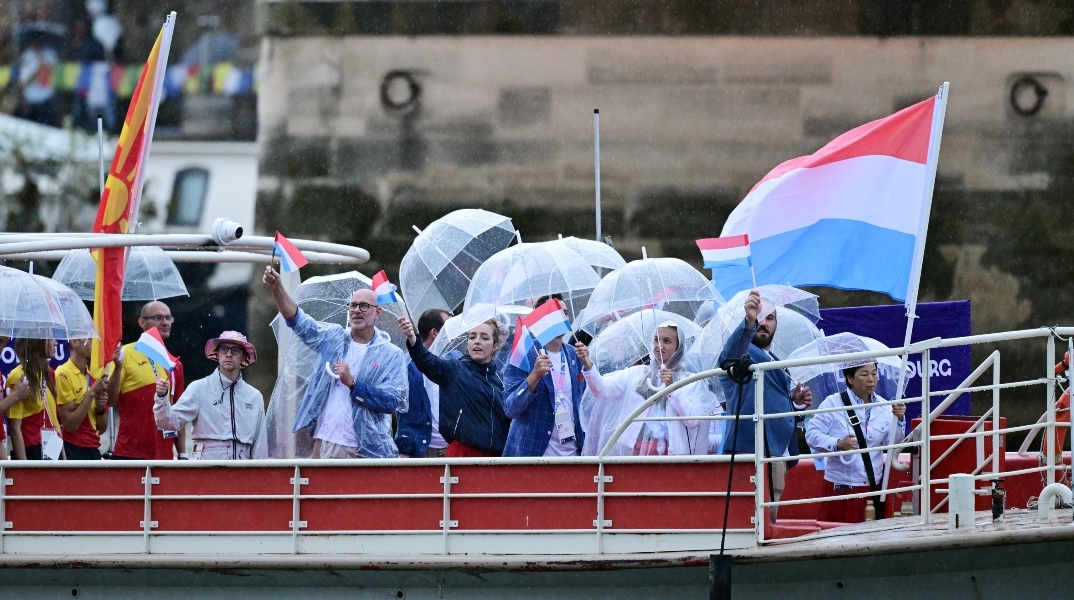 γαλλοι αθλητες σε βαρκα με αδιαβροχα, σημαιες και ομπρελες