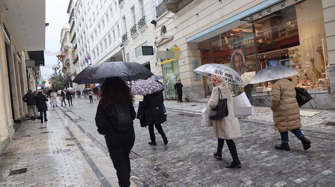 Πολίτες με ομπρέλες περπατούν υπό βροχή στην Ερμού